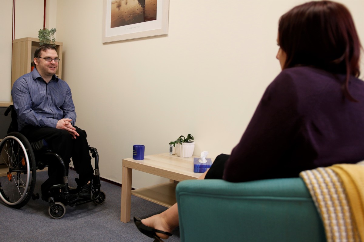A man in a wheelchair is talking to a woman in a Living Options Devon meeting room