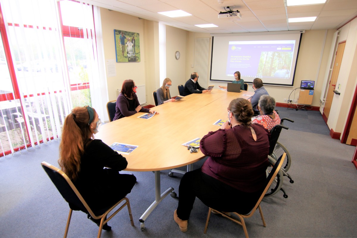 work colleagues sat around the conference table in the Swan meeting room at Living Options Devon offices.  Some of the people are wheelchair users