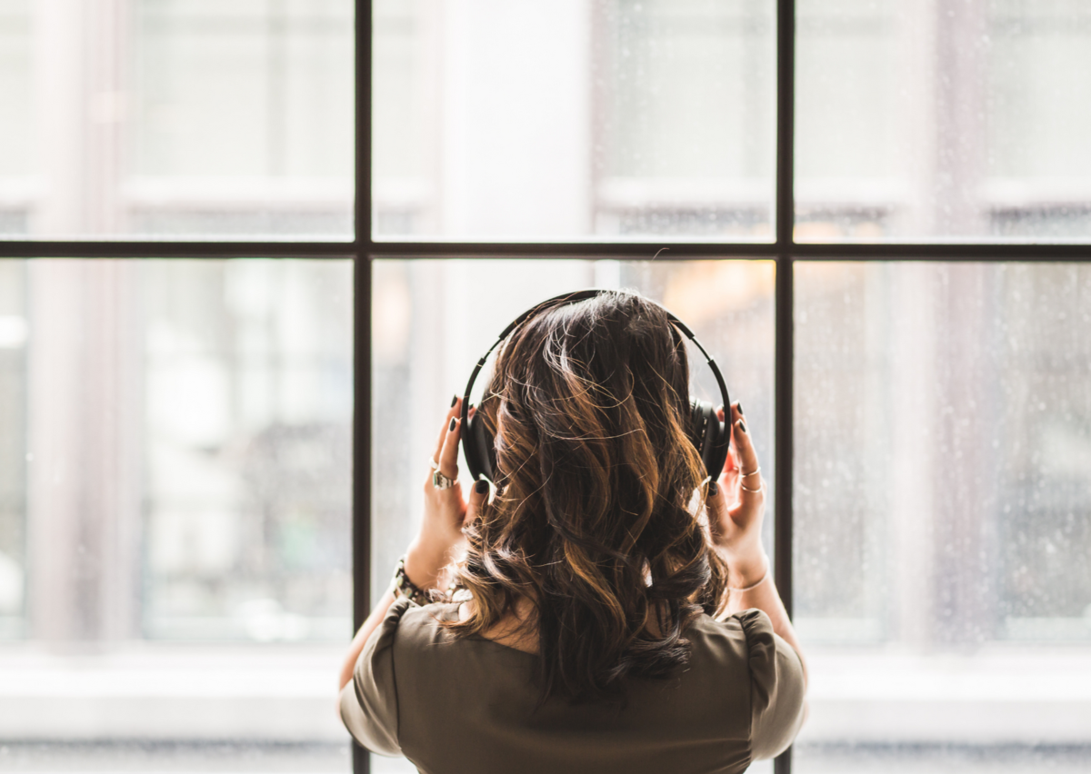 lady with back to camera looking out of a window wearing headphones and listening to audio message
